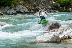 Kayaker navigating turquoise whitewater among rocks on a fast river.