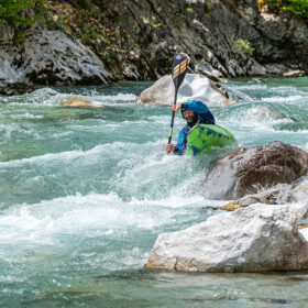Kayaker navigating turquoise whitewater among rocks on a fast river.
