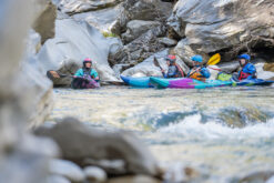 Group of kayakers in colorful boats navigating a rocky river gorge.