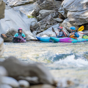 Group of kayakers in colorful boats navigating a rocky river gorge.",