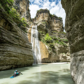 Person paddling a blue kayak through a narrow canyon with a waterfall overhead? Actually state no question mark.
