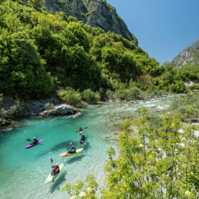 Turquoise river winds through a forested canyon with kayakers paddling on the water.