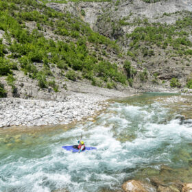 Kayaker navigating turquoise rapids along a rocky canyon with greenery on the cliffs.