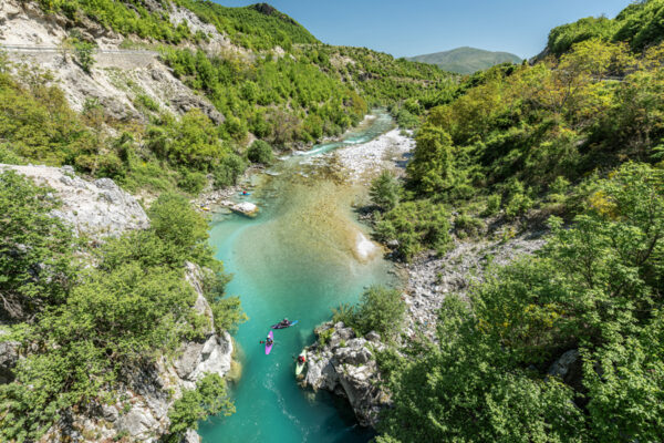 Turquoise river winding through a green forested canyon with kayakers paddling along rocky banks.