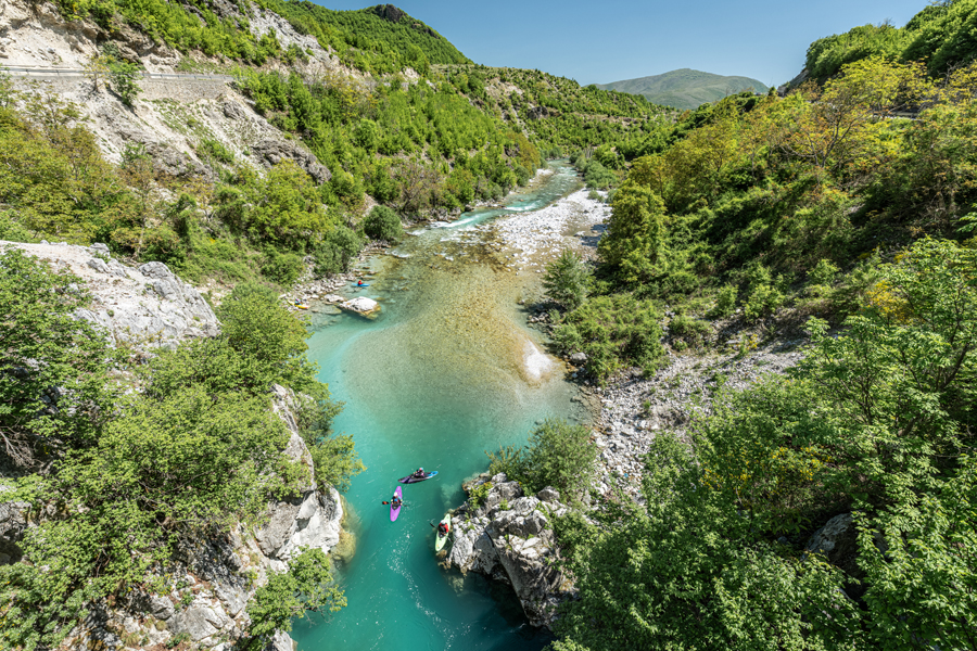 Turquoise river winding through a green forested canyon with kayakers paddling along rocky banks.