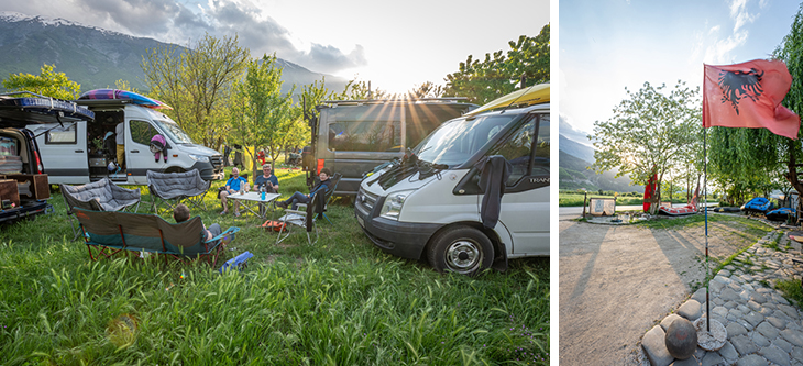Sunny campsite with camper vans and a group of people seated in lawn chairs around a picnic table, mountains in the background.