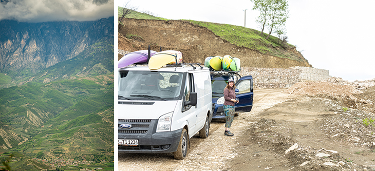 White van with colorful kayaks on its roof and a person standing by the open door on a dirt lot, with mountains in the distance on the left.