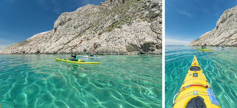 Two kayakers in bright yellow kayaks paddle near a rocky coastal cliff under a clear blue sky; turquoise water.
