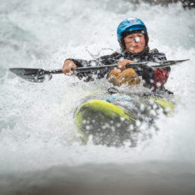Kayaker in a blue helmet paddling through whitewater spray.